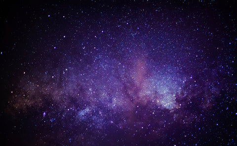 A star-filled night sky with the Milky Way galaxy glowing in shades of purple, blue, and black.